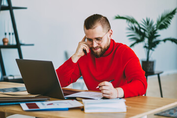 Young hipster guy making notes during telephone consultancy sitting at desktop,male freelancer...