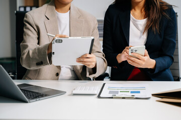 Business documents on office table with smart phone and calculator digital tablet and graph business with social network diagram and two colleagues discussing data working