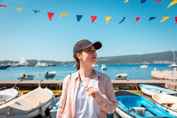 Pretty young Caucasian woman in cap and shirt stands on dock, fearing sunstroke. Summer heat at...