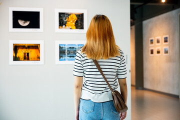 Asian woman standing she looking art gallery in front of colorful framed paintings pictures on...
