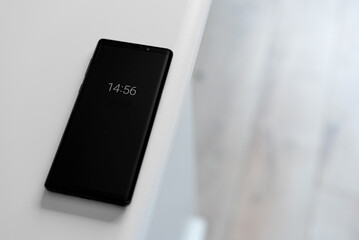Black smartphone on a white table. Clock numbers on the screen.