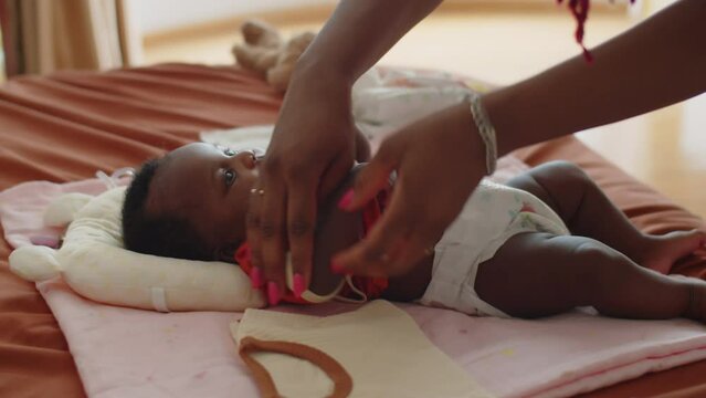 Cropped shot of hands of caring mother changing clothes on little daughter lying on blanket