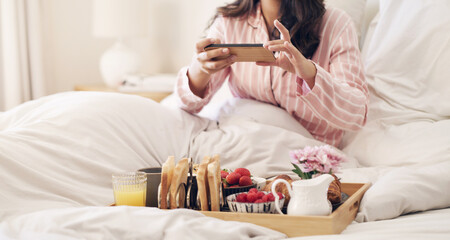 Phone, bed and food in hotel, person and digital for photography, social media and relax in...