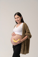 Portrait of Beautiful pregnant woman holding banana over white background studio, health and maternity concept.