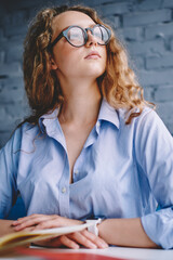 Caucasian woman in trendy eyewear for vision correction thoughtful on information from textbook for...