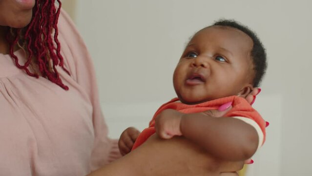 Handheld shot of African American mother with red dreadlocks spending time with cute newborn daughter at home