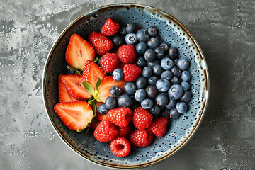 A ceramic bowl adorned with vibrant slices of strawberries, raspberries, and blueberries, creating an enticing and colorful fruit arrangement.