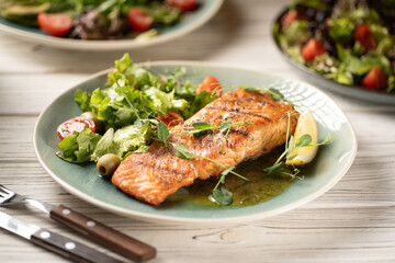 One piece of salmon grilled with lettuce and vegetables salad. Serving dishes on table
