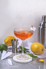 Paper plane boozy alcohol cocktail with Bourbon, whiskey, amaro, aperol aperitif, fresh lemon juice and paper plane craft made decor, on white background with hard light and bar utensils