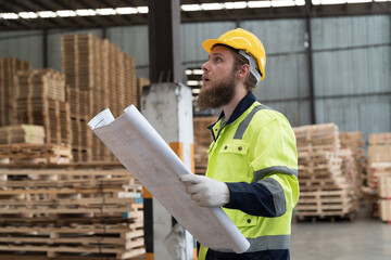 Male warehouse worker working and holding blueprint structure of building in wooden warehouse...