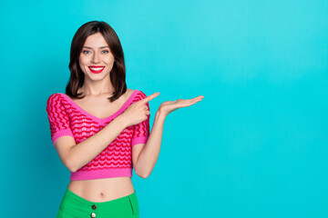 Photo of toothy beaming cute woman dressed knitwear top indicating at object on palm empty space isolated on blue color background