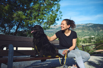 Cute black cocker spaniel dog sitting near his family on the bench in mountains nature