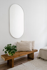 Bedroom with pilea houseplant and cushion on wooden bench under mirror