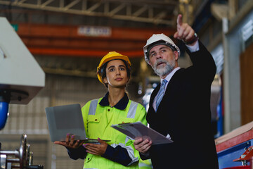 Two people are looking at a laptop, one of them is wearing a yellow jacket. Scene is serious and focused to machine controller board in factory.