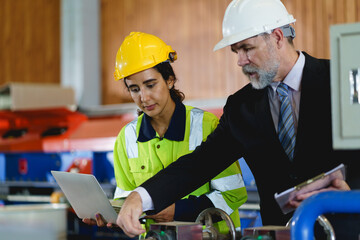 Two people are looking at a laptop, one of them is wearing a yellow jacket. Scene is serious and focused to machine controller board in factory.