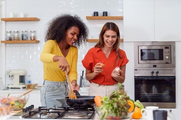 A couple of young girls friends laughing and having fun while cooking, Happy LGBT lesbian couple ...