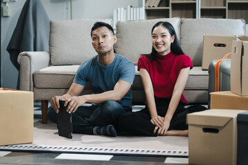 Young couple relaxing sitting on the floor around cardboard boxes at home, smiling happy moving to...