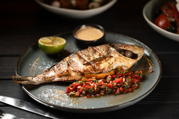 Grilled whole dorado fish served with vegetables, sauce and lemon on a blue plate. Seafood food