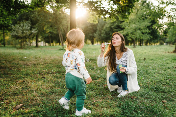 Mom blow soap bubbles outdoor. Toddler little cute walking and playing in spring garden. Boy...