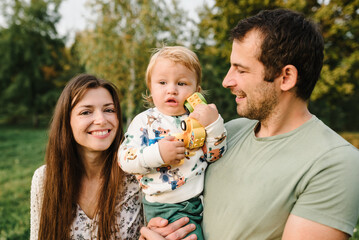 Kid hugging parents happiness playing in green grass in park. Happy mother, father hug baby son walking in garden at sunset. Family spending time together outdoors. Children's day. Friendly family.