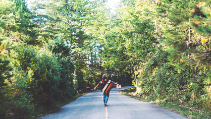 Young woman travel nature. She walking on asphalt road in forest pine green and write a note among...