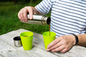 A man on the street pours coffee from a thermos into a green cup, enjoying his outdoor recreation.