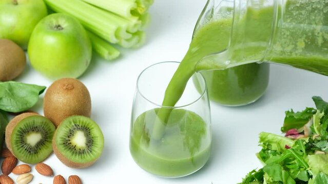 Green smoothie of celery, kiwi, green apple and spinach pouring into a glass, slow motion.