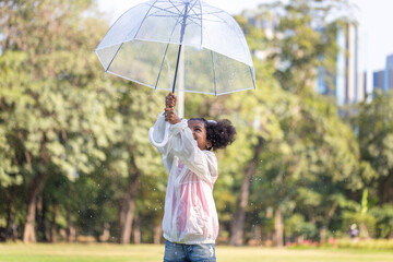 Child girl with an umbrella playing with rain in the park, Little kid girl playing outdoors in the garden