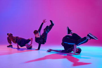 Energetic photo of talented boys, in black attire dancing hip-hop in motion in mixed neo n light against vibrant gradient background. Concept of sport and hobby, music, fashion and art, movement. Ad
