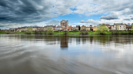 Obraz premium Paisaje Urbano con Río y Cielo Nublado: Reflejo Natural y Arquitectura. Ciudad de Moulins sur allier