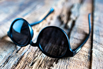 round stylish sunglasses on a textured wooden background.