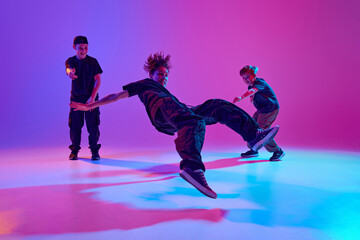 Talented boys in sports attire performing hip-hop moves in mixed neon light against vibrant...