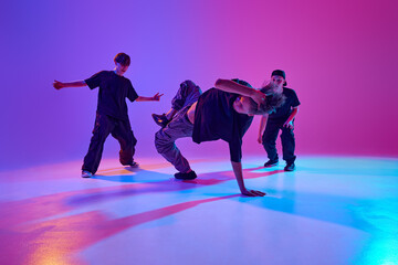 Three young male dancers participate in street dance battle in mixed neon light against vibrant gradient background. Concept of sport and hobby, music, fashion and art, movement. Ad