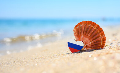Sandy beach in Russia. Russian flag in the shape of a heart and a large shell.