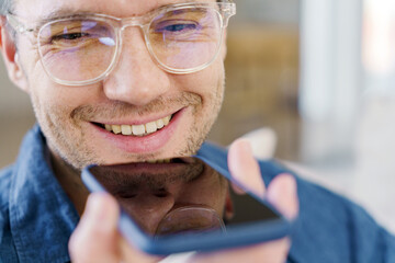A close-up of a cheerful young man using voice commands on his smartphone, showcasing his enjoyment...