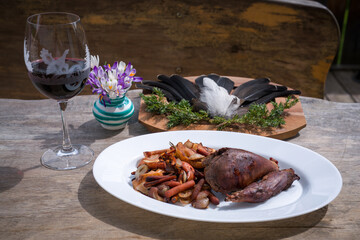 happy hunting, ready to eat - grilled game meat from a black grouse from the charcoal grill with apples,  carrots, onions and a glas of red wine at a sunny spring day