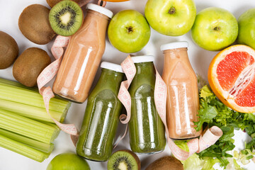 Healthy bottled smoothies among vegetables and fruits and measuring tape.