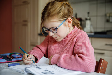 Portrait of happy little girl doing homework at home. Elementary school studing writing and learning. Smiling child writing letters, learing to write.