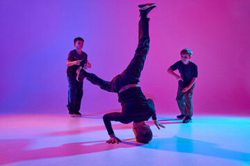 Neon dance battle. Dancer performing impressive headstand, breakdance moves in mixed neon light...