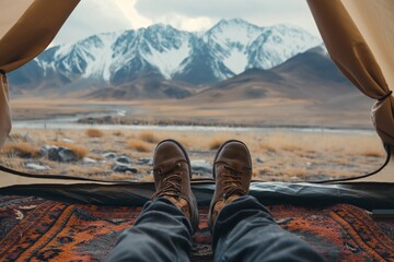 View from a tent of a persons feet with snowy mountains and a vast plain in the background