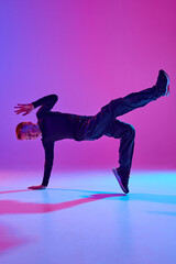 Talented young boy in black attire, street dancer performing tricks in mid-air in mixed neon light against vibrant gradient background. Concept of sport and hobby, music, fashion and art, movement. Ad