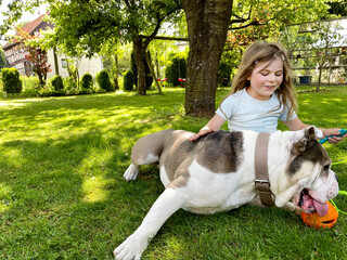 Cute little toddler girl playing with family dog in garden. Happy smiling child having fun with...