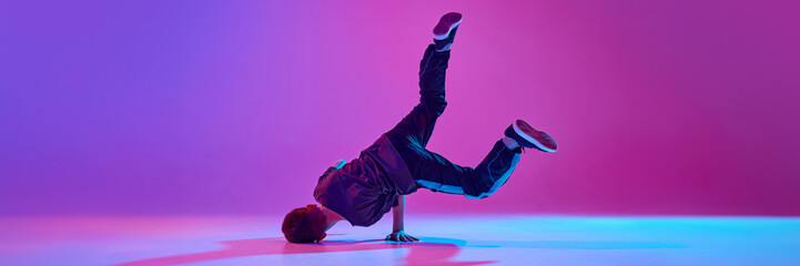 Banner. Teenager, break-dancer spinning on head in motion in mixed neon light against vibrant gradient background. Copy space. Concept of sport and hobby, music, fashion and art, movement. Ad