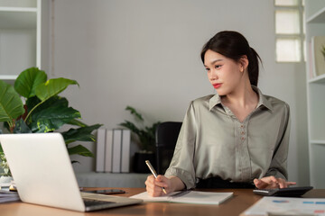 Business woman working in office checking documents. Woman accounting executive using laptop reading paper file financial report, tax invoice