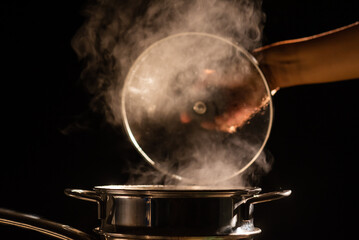 A boiling pot steams up as a chef opens the lid of a cooking steam pot in a restaurant.	