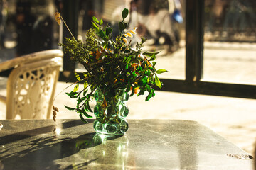 Glass transparent green modern vase with plants and blooming flowers on a table on a terrace of a...