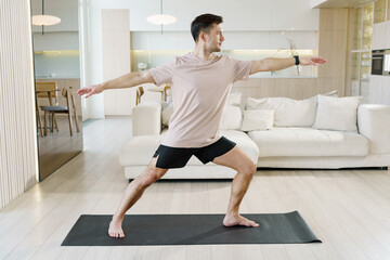 A man practices the yoga pose with focus and strength, positioned on a yoga mat in a bright and...