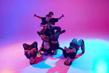 Group of young male dancers posing and showing acrobatic formation in mixed neon light against...