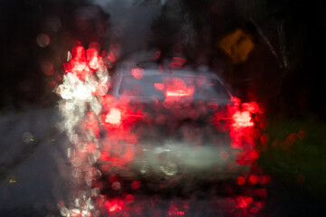 Abstract image of white headlights and red car taillights viewed through a wet windshield.