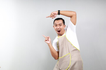 Asian Waiter in brown apron checking out promo offer, pointing finger and looking left at your...